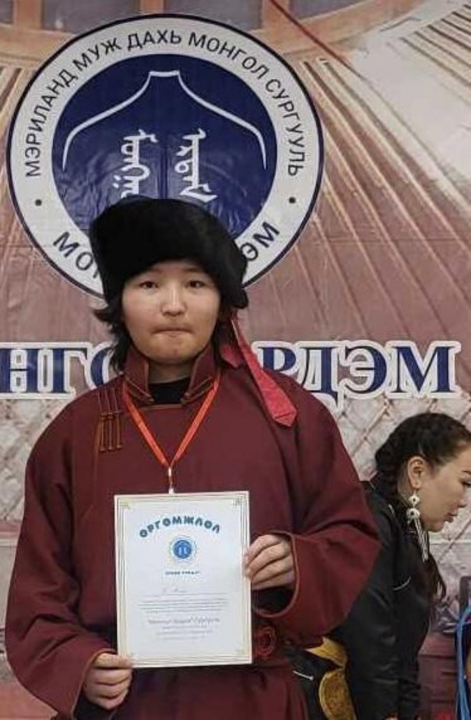Anand in a maroon deel and fur hat holding a Student of the Year certificate